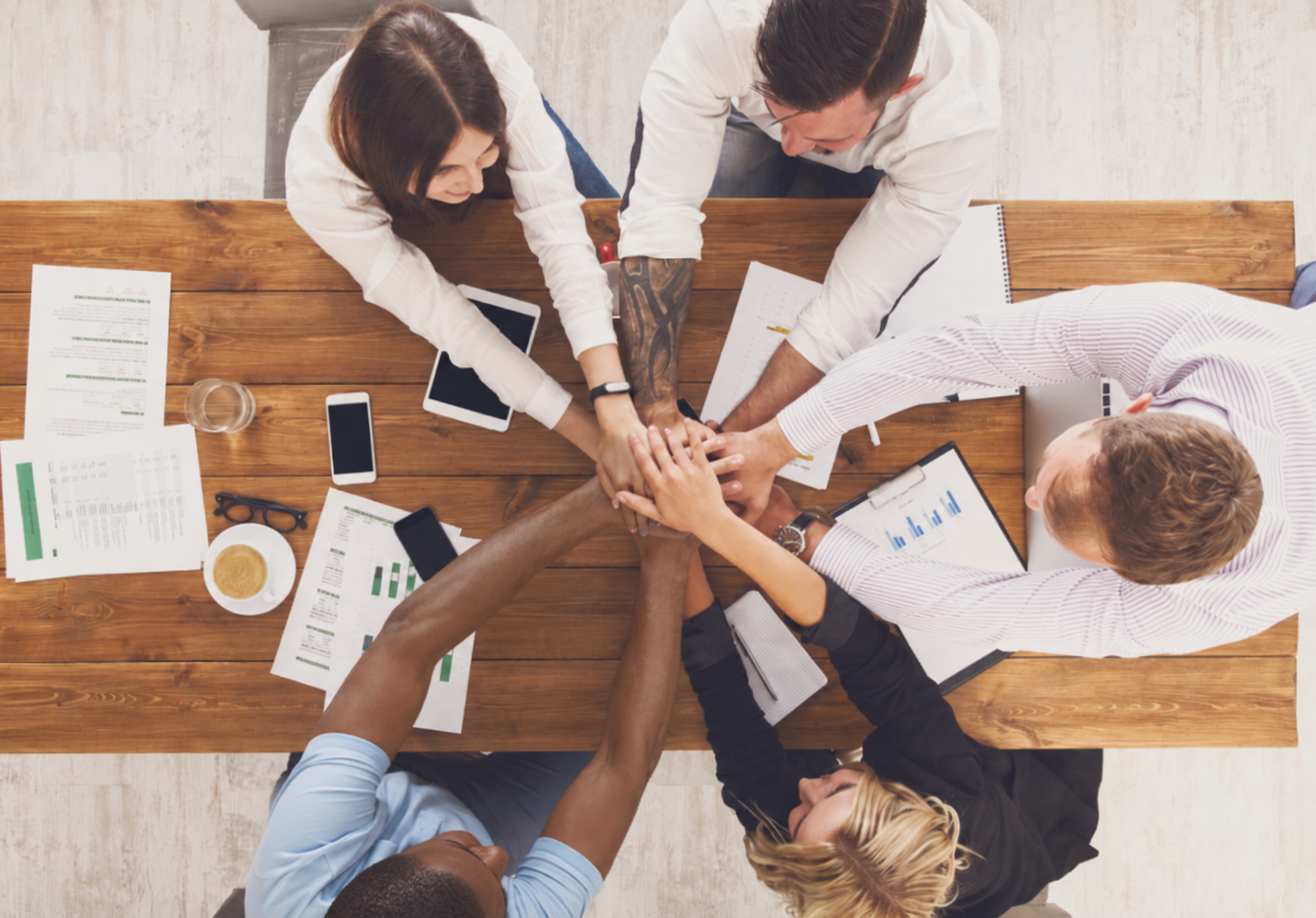 A diverse small business team stacking their hands together around a meeting table